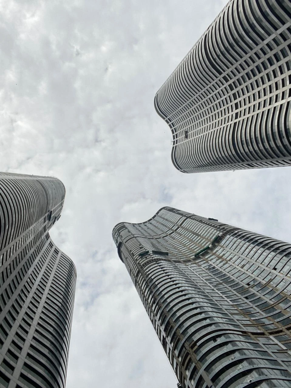 Looking up at three curved residential towers of Lodha World Towers, Mumbai, against a cloudy sky